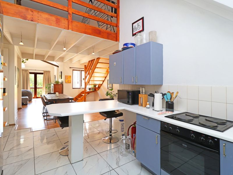 Open-plan kitchen and living area featuring tiled floors, built-in cabinetry, and a wooden staircase leading to a mezzanine level.
