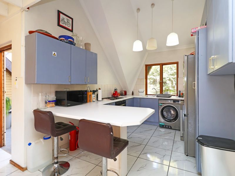 A functional kitchen featuring built-in cabinetry, tiled flooring, and a breakfast bar, with integrated appliances and natural light from the window.