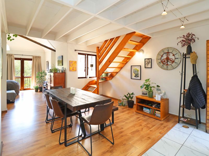 Open plan living and dining area featuring exposed beam ceilings, a wooden staircase, and a seamless transition to an outdoor balcony space.
