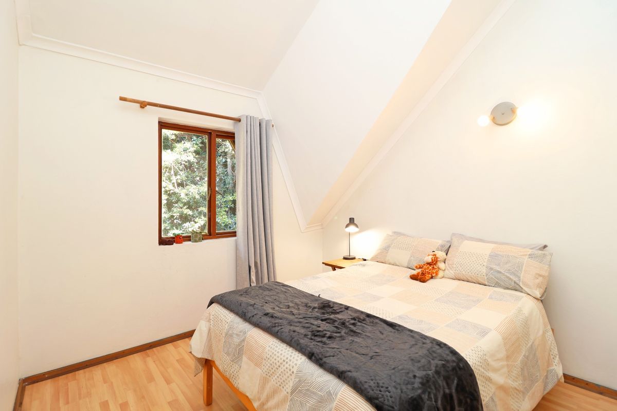 A cozy bedroom featuring laminate flooring, a sloped ceiling, and a timber-framed window overlooking greenery.
