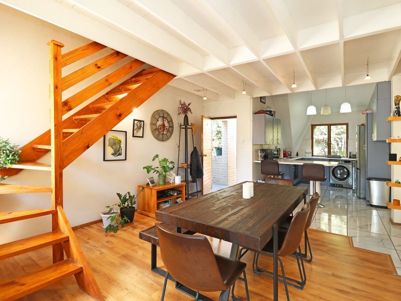 Open plan living and dining area featuring a wooden staircase, exposed beam ceiling, and a functional kitchen with breakfast bar and tiled flooring.