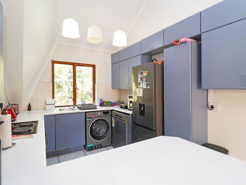 A functional kitchen featuring blue cabinetry, a tiled backsplash, integrated hob, and space for laundry appliances under the counter.