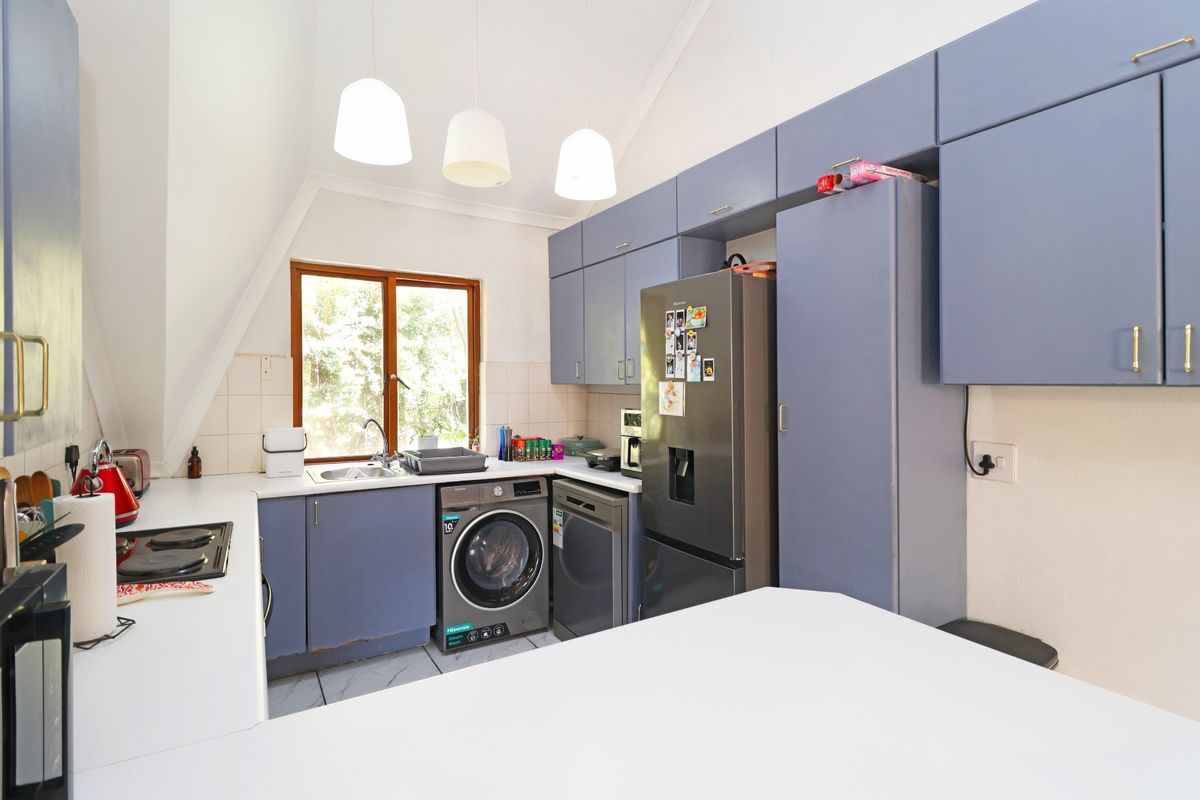 A functional kitchen featuring blue cabinetry, a tiled backsplash, integrated hob, and space for laundry appliances under the counter.