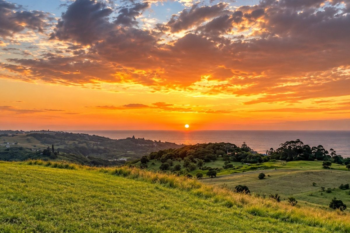 A scenic landscape view of rolling green hills overlooking the ocean at sunset.