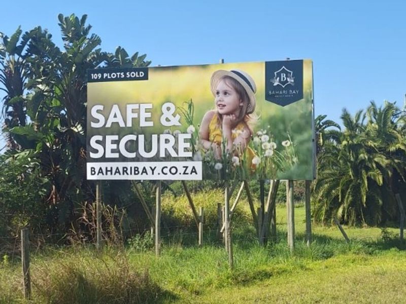 A large promotional billboard situated on a vacant residential plot, highlighting the security and development status of the Bahari Bay estate.