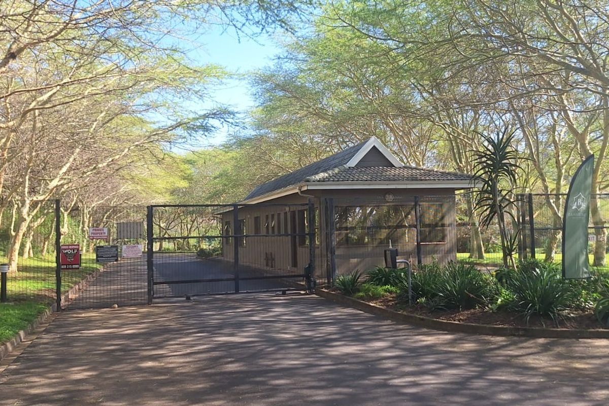A secure gated entrance to the residential estate featuring a guard house, perimeter fencing, and a well-maintained paved driveway.