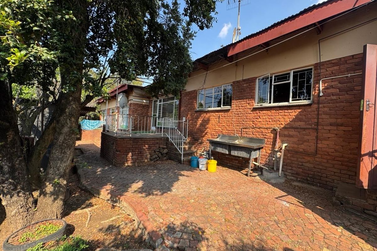 Rear exterior view of a brick house featuring a paved patio, raised terrace with metal railing, and an external utility sink area.