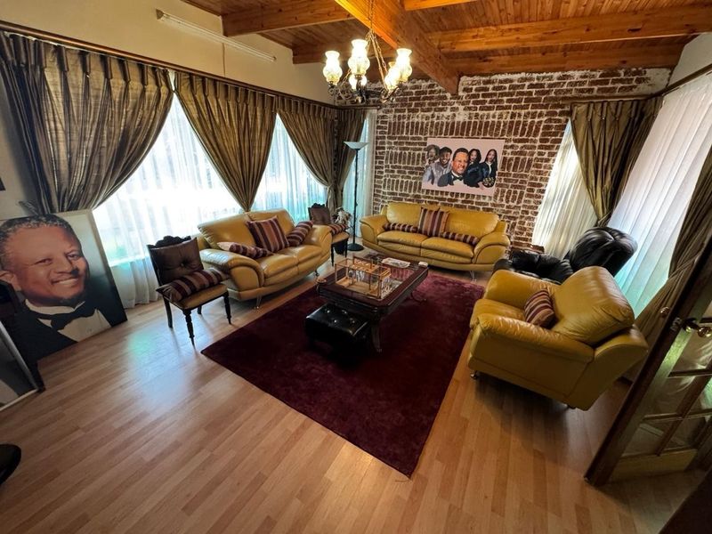 Spacious living room featuring a rustic exposed brick wall, high timber-beamed ceilings, and light-toned laminate flooring, creating a warm and character-filled atmosphere.