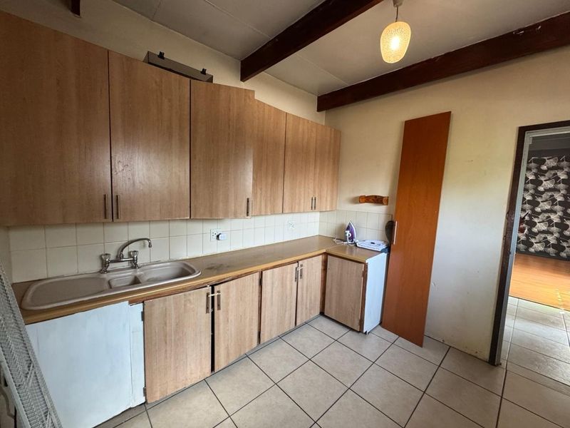A functional kitchen featuring laminate cabinetry, tiled flooring, and exposed timber ceiling beams, offering a blank canvas for potential renovation and modernization.