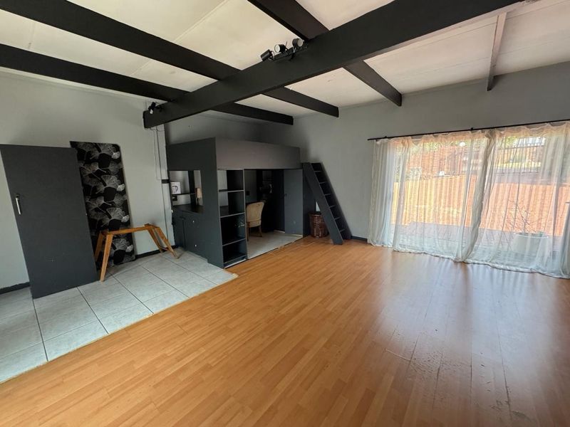 Spacious living area featuring exposed ceiling beams, laminate flooring, and a unique built-in loft structure with direct access to the outdoor area.