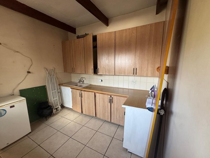 A functional laundry area featuring laminate cabinetry, a tiled backsplash, stainless steel sink, and ceramic floor tiles with exposed ceiling beams.