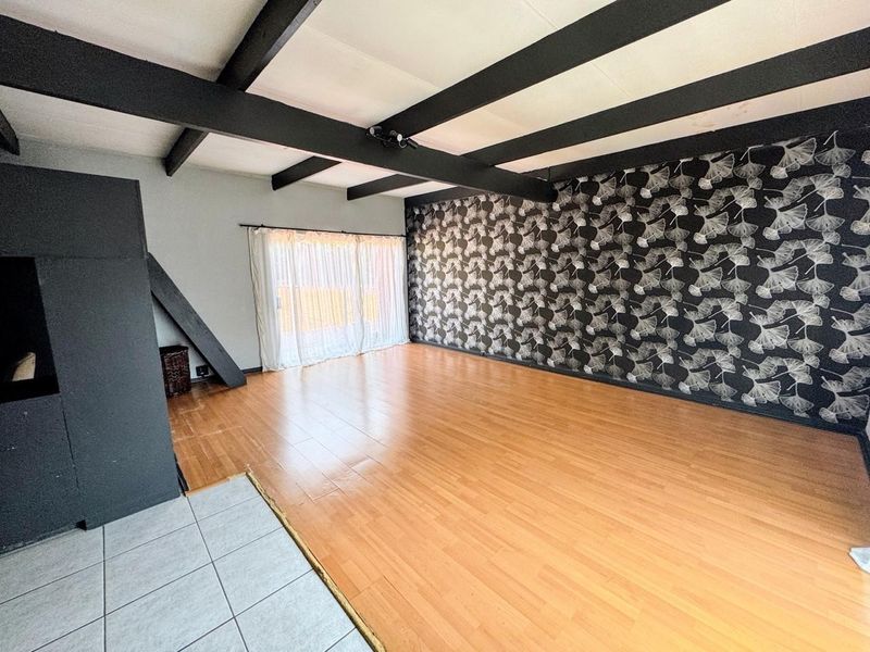 Spacious living area featuring exposed ceiling beams, a mix of laminate and tiled flooring, and a large sliding door providing natural light.