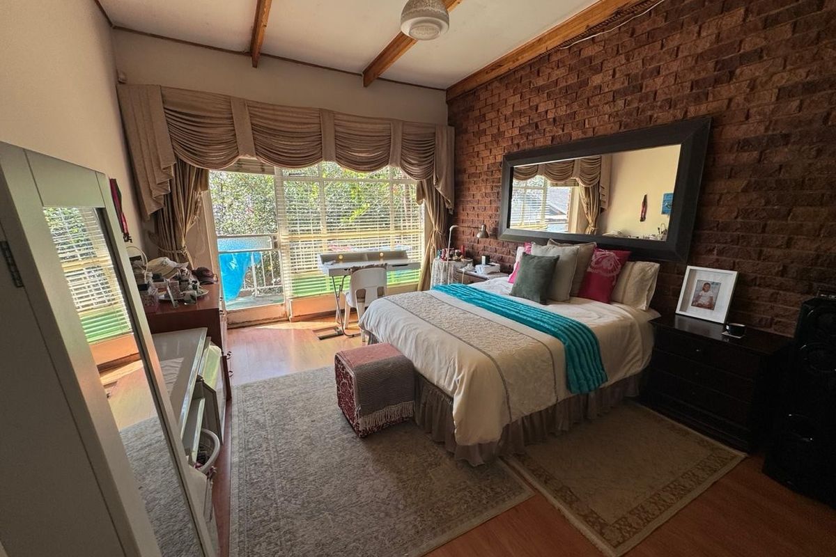 Spacious bedroom featuring an exposed brick feature wall, timber ceiling beams, and a sliding glass door providing access to an outdoor area.