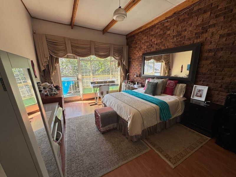 Spacious bedroom featuring an exposed brick feature wall, timber ceiling beams, and a sliding glass door providing access to an outdoor area.