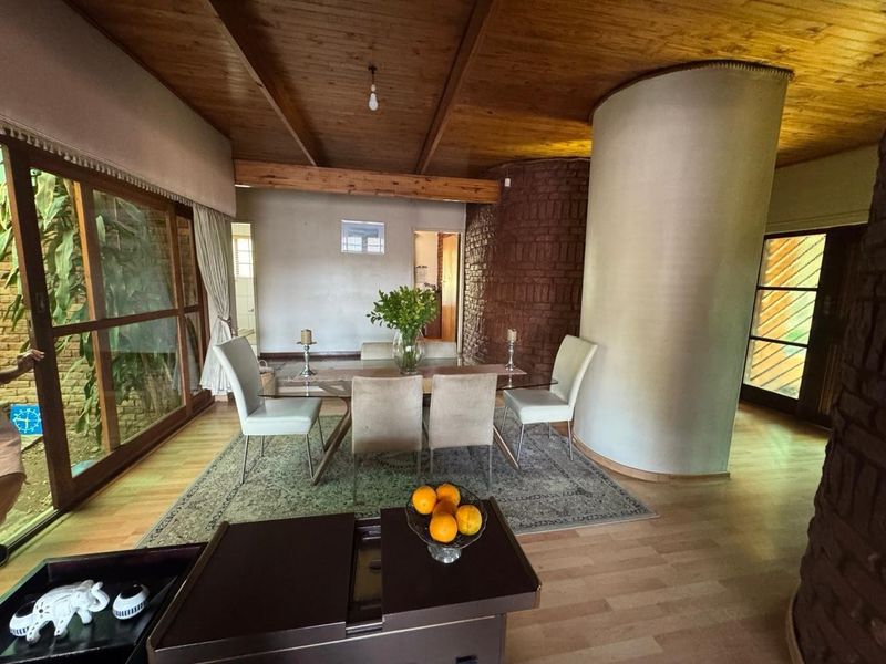 Dining area featuring a unique curved architectural column, exposed brick wall, and timber beam ceiling with large sliding doors providing natural light.