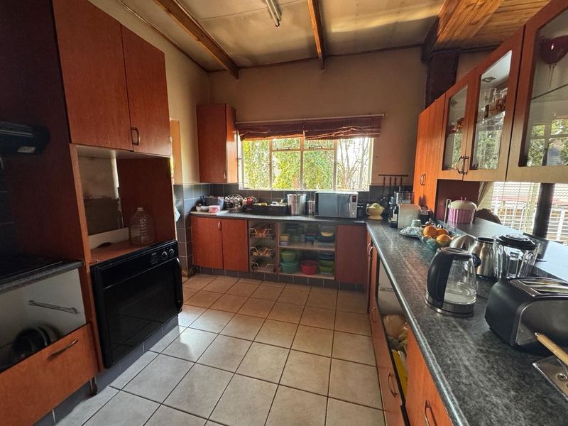 A functional kitchen featuring wooden cabinetry, tiled flooring, built-in oven, and exposed timber ceiling beams, offering a classic layout with ample storage space.