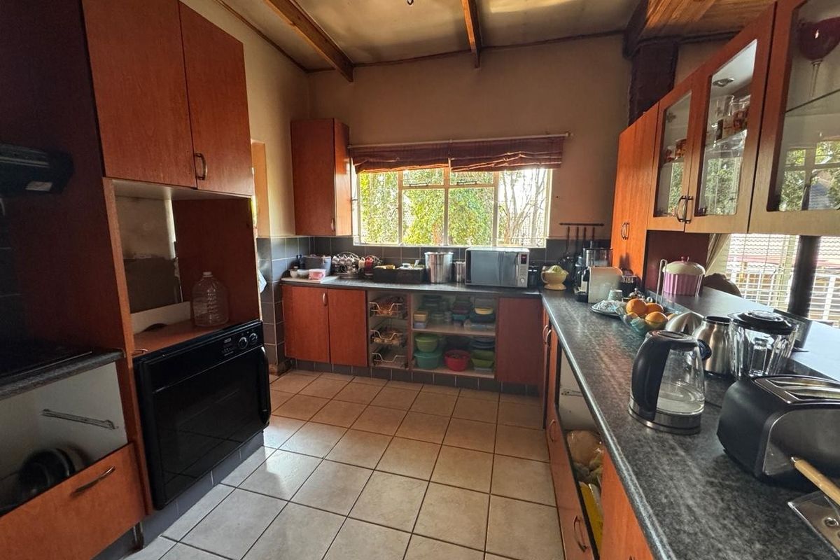 A functional kitchen featuring wooden cabinetry, tiled flooring, built-in oven, and exposed timber ceiling beams, offering a classic layout with ample storage space.