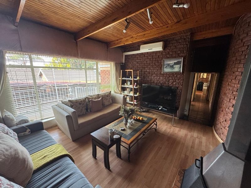 A cozy living room featuring exposed brick walls, a timber beam ceiling, laminate flooring, and a built-in wood-burning fireplace.