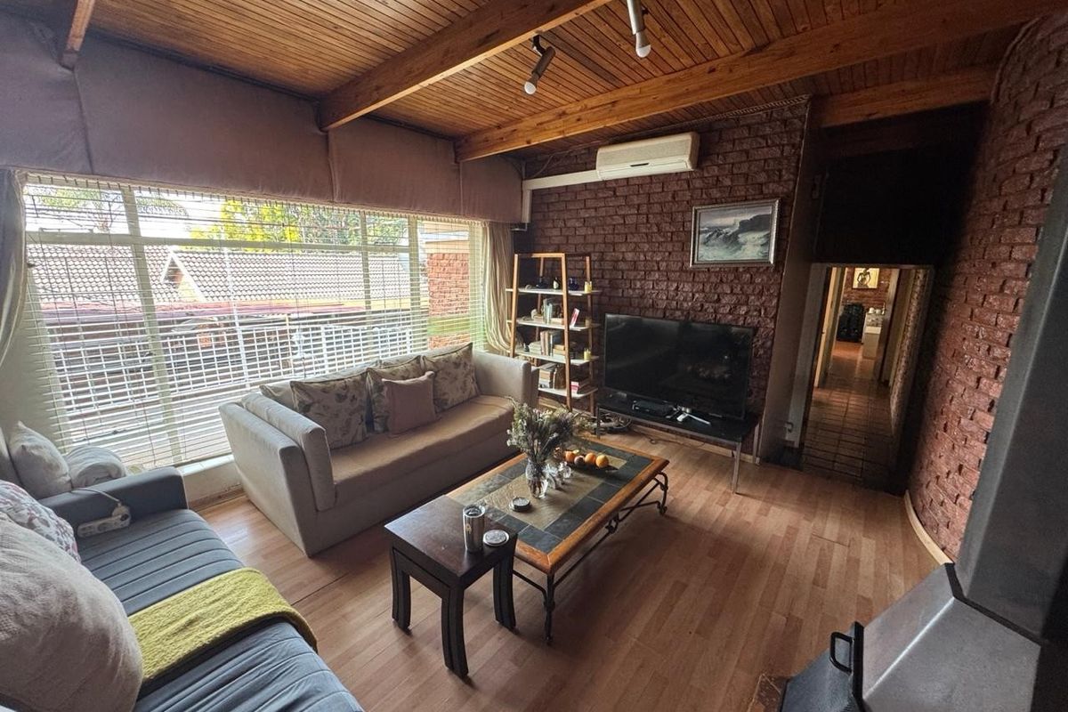 A cozy living room featuring exposed brick walls, a timber beam ceiling, laminate flooring, and a built-in wood-burning fireplace.