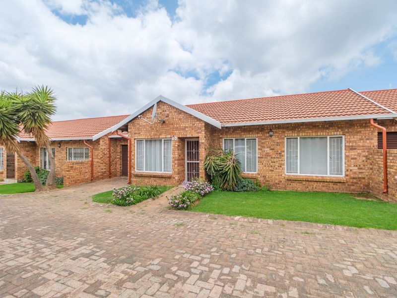 Front elevation of a face brick townhouse featuring a tiled roof, paved driveway, and established garden area.