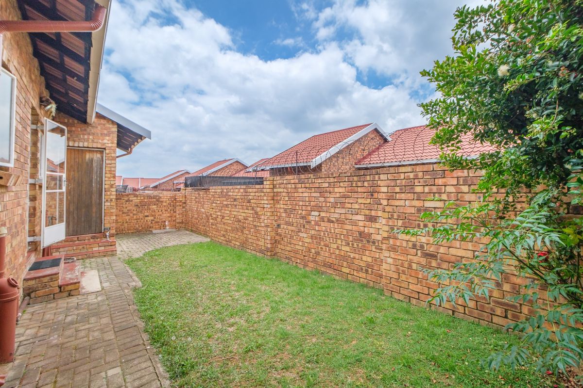 A private rear garden featuring a paved patio area, a small lawn, and high face brick boundary walls with security spikes.