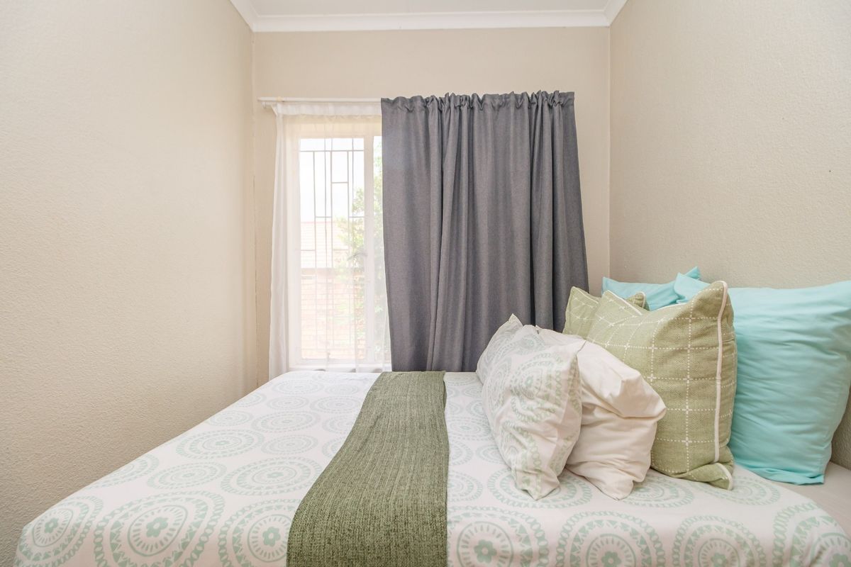 A cozy bedroom featuring neutral walls, coving, and a window fitted with security bars, providing a functional and comfortable living space.