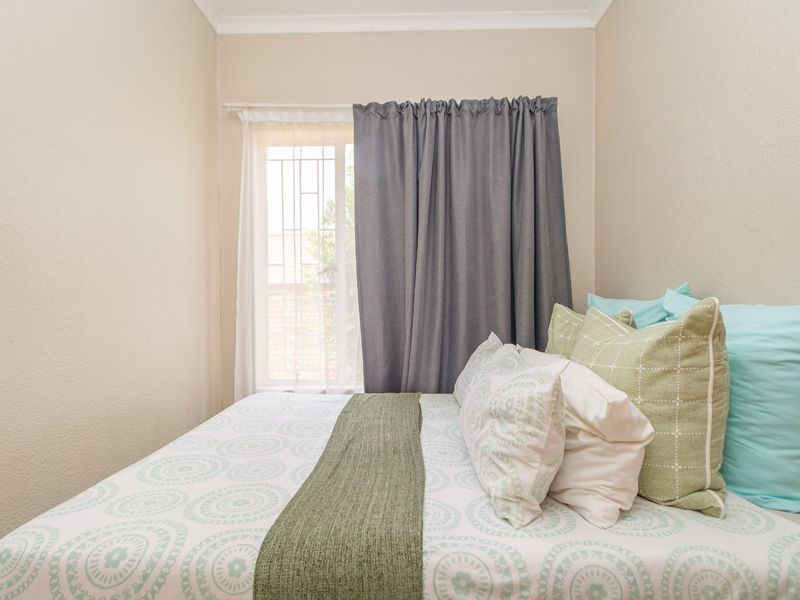 A cozy bedroom featuring neutral walls, coving, and a window fitted with security bars, providing a functional and comfortable living space.