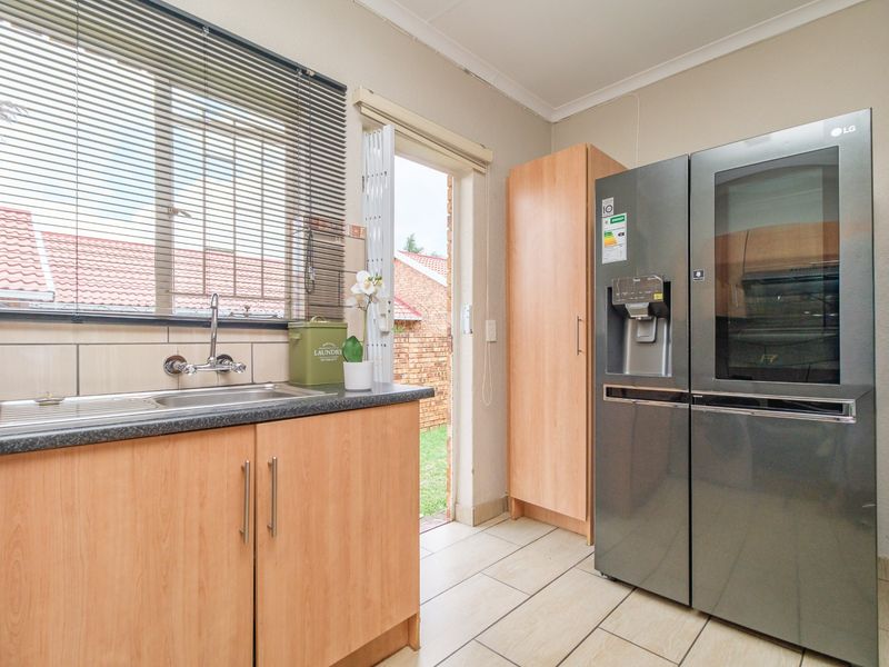 A functional laundry area featuring laminate cabinetry, a stainless steel sink, tiled flooring, and direct access to the rear exterior.