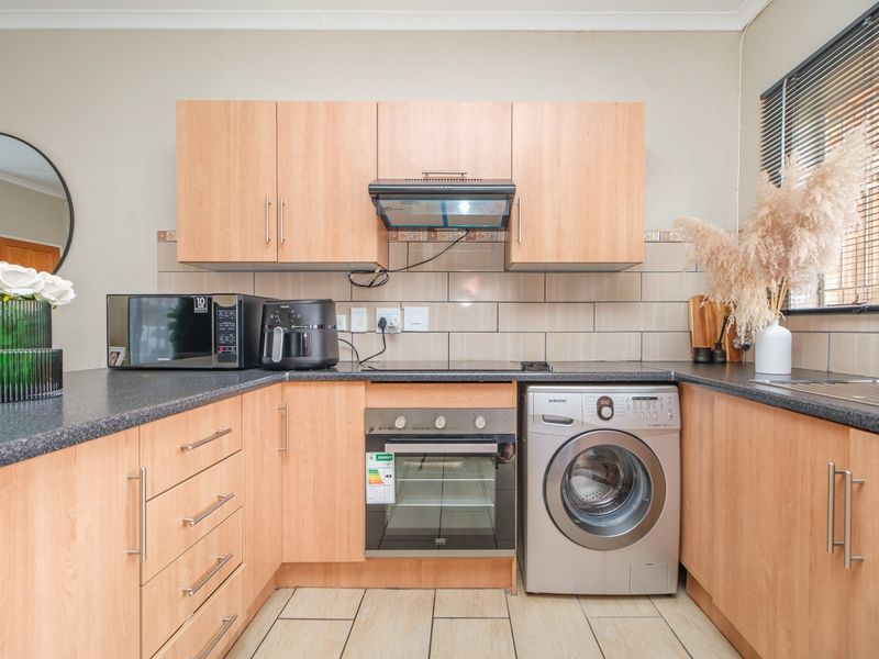 A functional kitchen featuring light wood-finish cabinetry, dark countertops, a built-in oven, extractor fan, and tiled flooring with a neutral backsplash.
