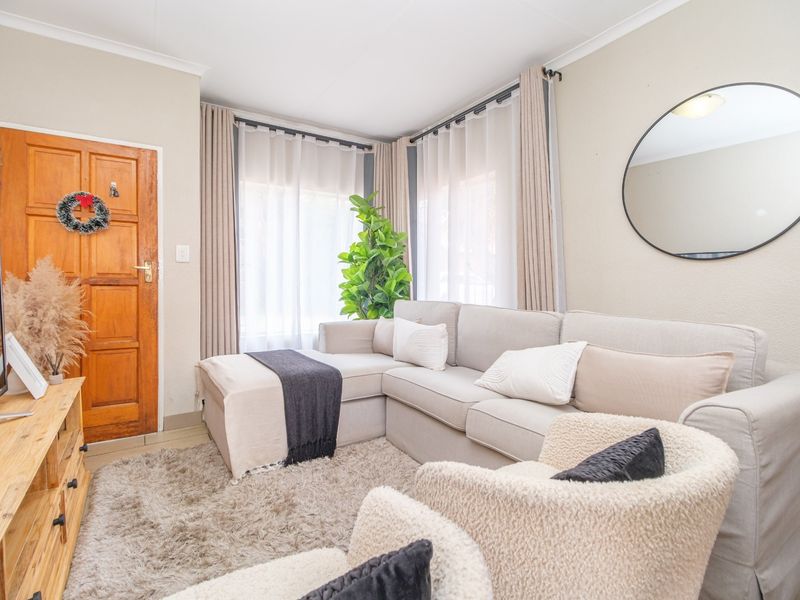 A bright living room featuring a timber entrance door, corner windows with curtain tracks, and neutral wall finishes.