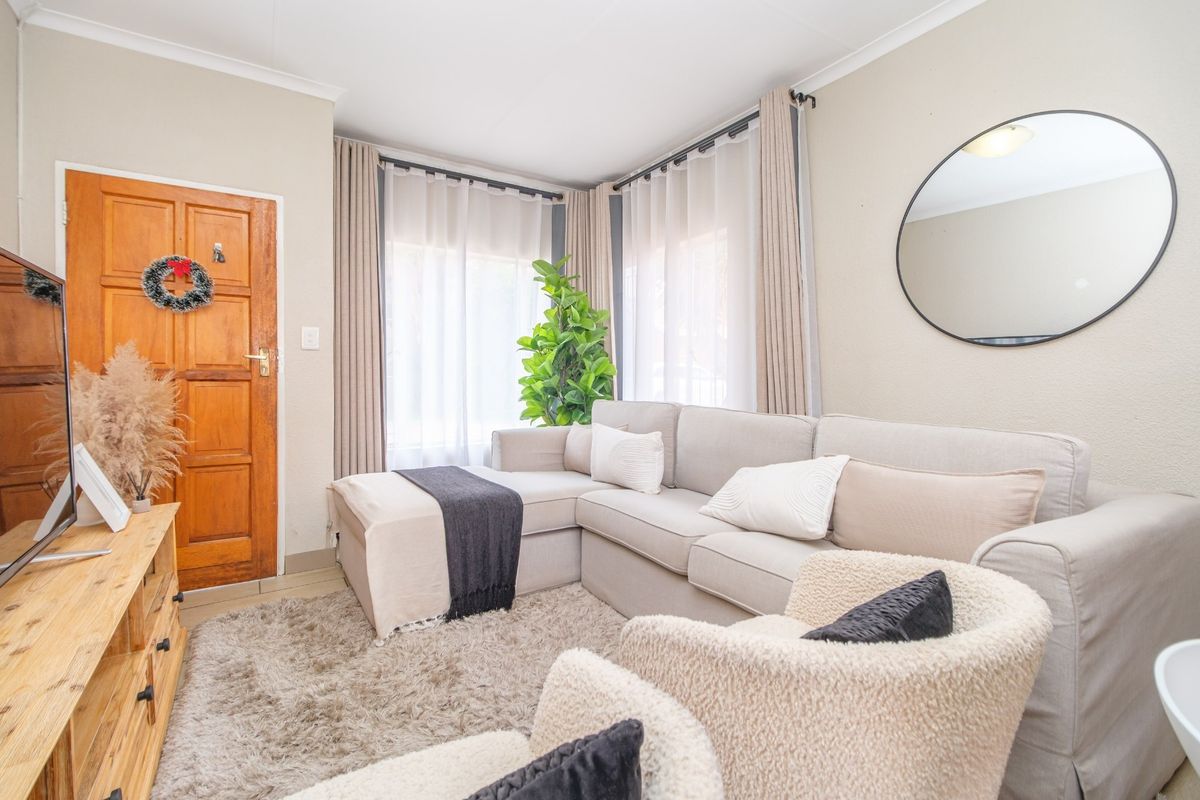A bright living room featuring a timber entrance door, corner windows with curtain tracks, and neutral wall finishes.