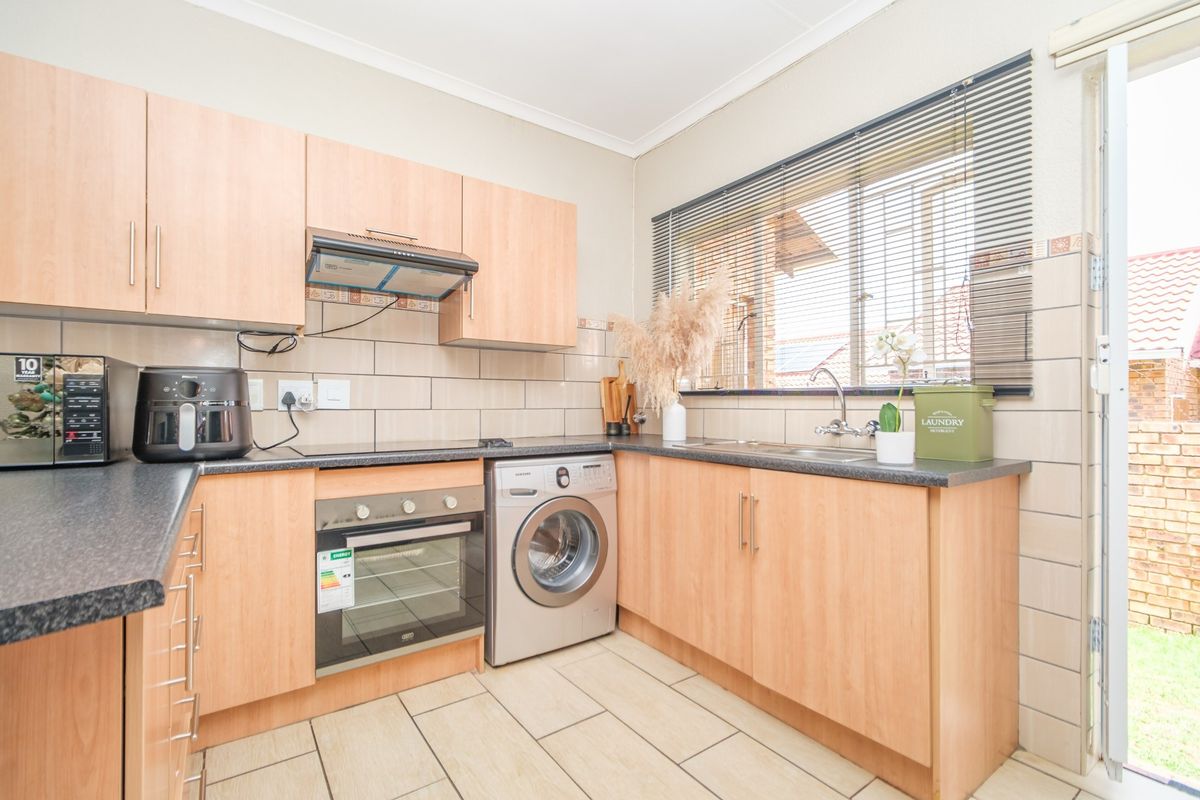 Functional kitchen featuring light wood-finish cabinetry, dark laminate countertops, built-in oven, extractor fan, and tiled backsplash with direct access to the exterior.