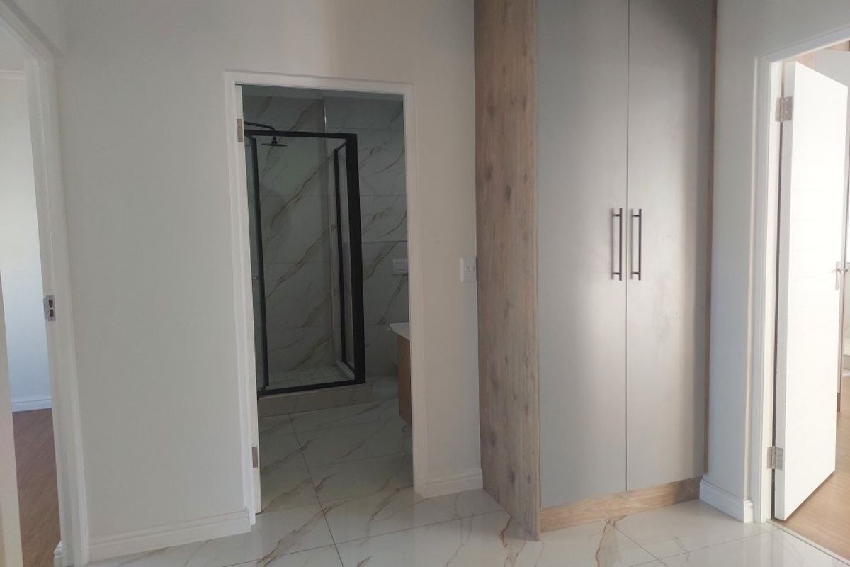 A modern bedroom featuring sleek built-in cupboards, polished marble-look floor tiles, and direct access to a contemporary en-suite bathroom with a shower.