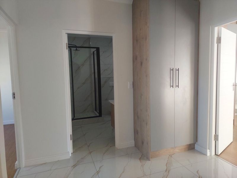 A modern bedroom featuring sleek built-in cupboards, polished marble-look floor tiles, and direct access to a contemporary en-suite bathroom with a shower.