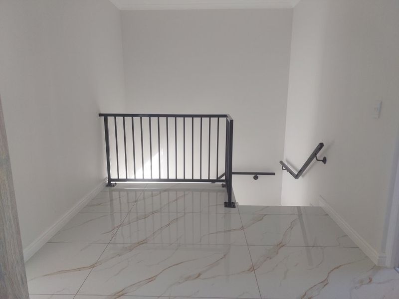 A bright, modern landing area featuring high-quality marble-look floor tiles and a sleek black metal balustrade with matching handrail.