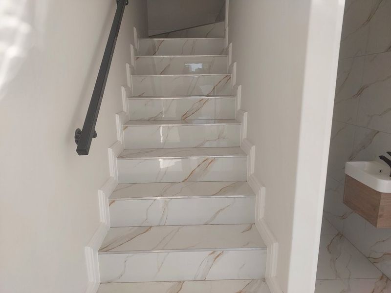 A modern staircase featuring marble-look tiled steps, a sleek black handrail, and clean white walls, leading to an upper level.