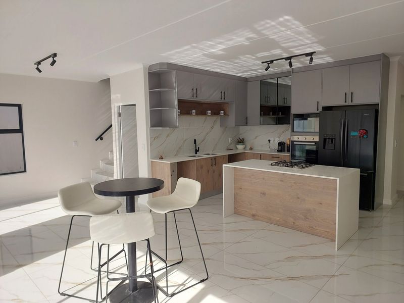 Modern open-plan kitchen featuring a central island with gas hob, sleek cabinetry, marble-look splashback, and high-quality porcelain floor tiles.