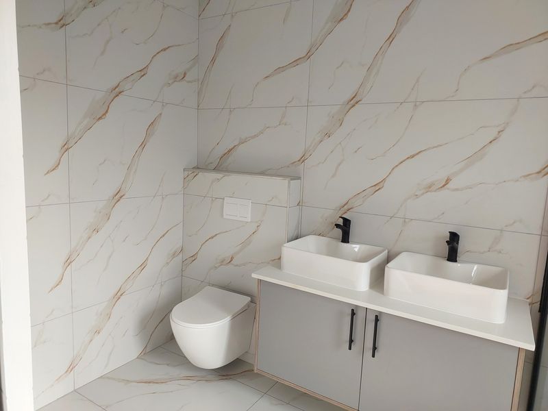 Modern bathroom featuring a dual vanity with vessel sinks, black fixtures, and elegant marble-effect wall and floor tiling.