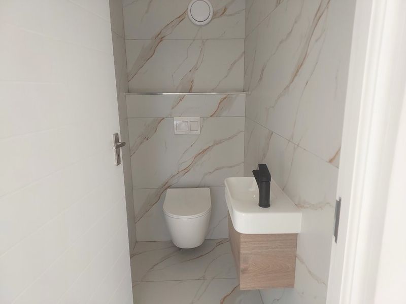 A modern, compact guest bathroom featuring marble-effect wall and floor tiles, a wall-hung toilet with a concealed cistern, and a floating vanity unit.