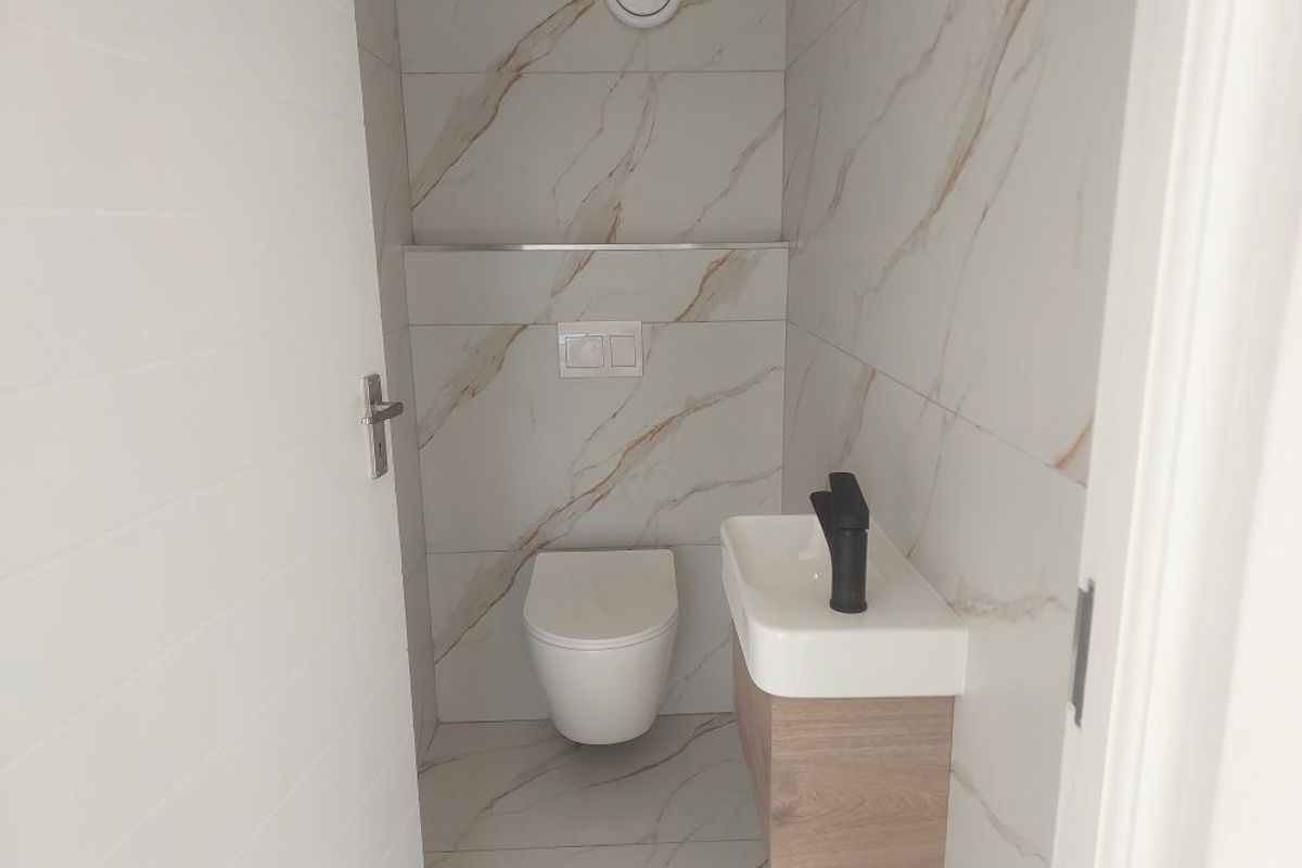 A modern, compact guest bathroom featuring marble-effect wall and floor tiles, a wall-hung toilet with a concealed cistern, and a floating vanity unit.