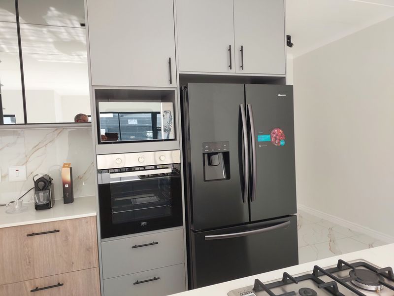 Modern kitchen featuring grey cabinetry, built-in oven and microwave, gas hob, and marble-look splashback with high-quality finishes.