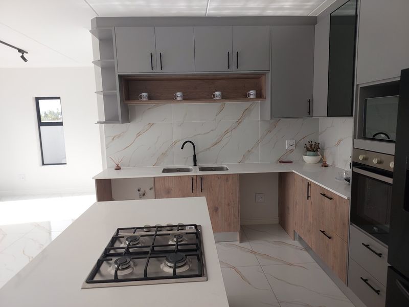 Modern kitchen featuring two-tone cabinetry, stone countertops, marble-look backsplash, integrated gas hob, and built-in oven with high-quality finishes.