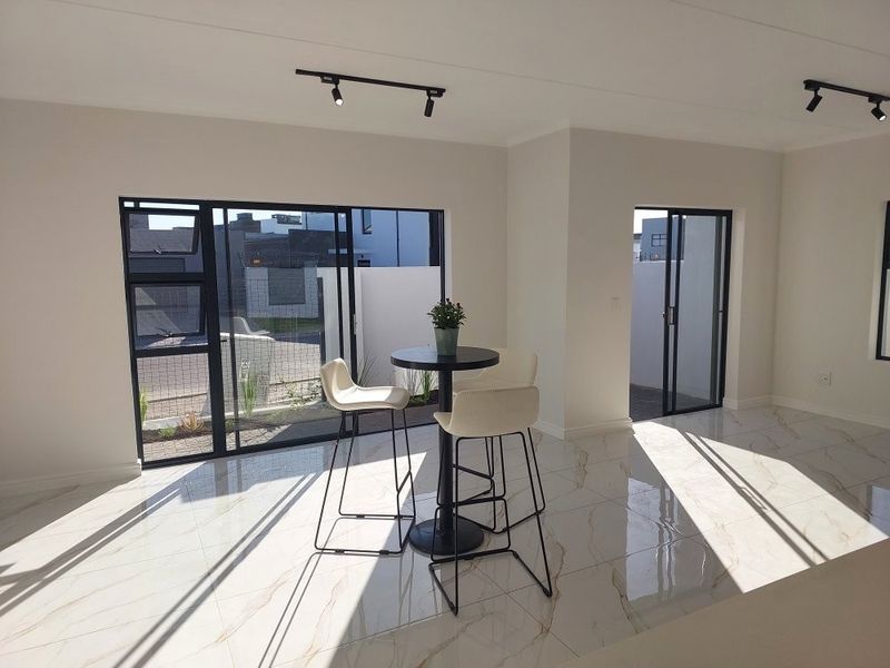 Bright open-plan living area featuring modern porcelain tile flooring, sleek black aluminium sliding doors, and contemporary track lighting.