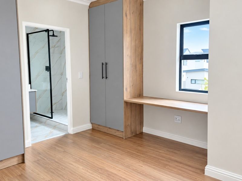 Modern bedroom featuring built-in cupboards, a integrated desk, laminate flooring, and an en-suite bathroom with a glass-enclosed shower.