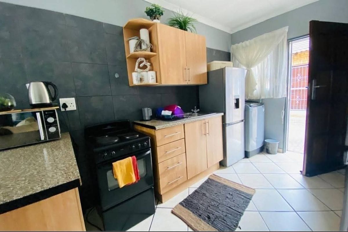 Compact kitchen featuring light wood cabinetry, granite countertops, a dark tiled backsplash, and a freestanding stove with direct access to the exterior.
