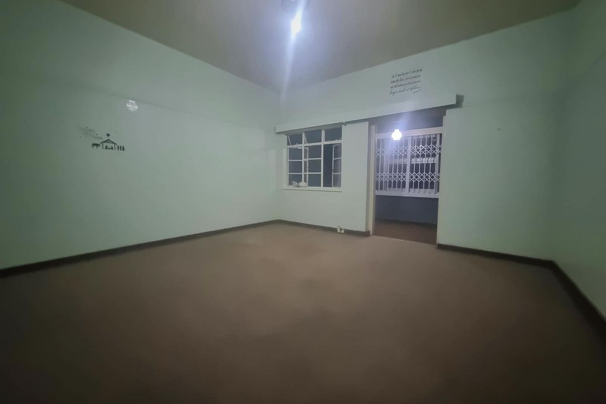 An empty, spacious living area featuring carpeted flooring and a security gate leading to an adjacent space.