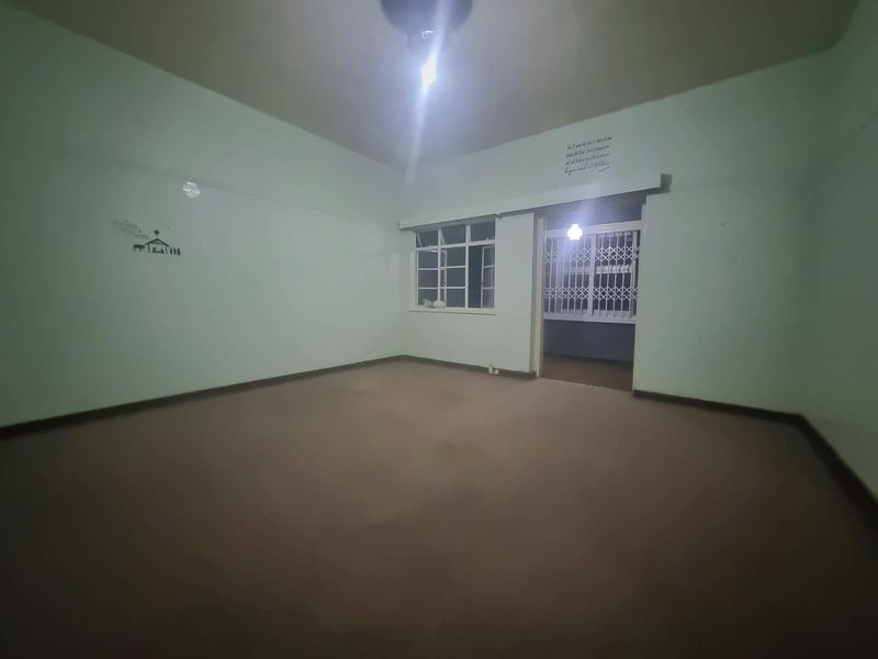 An empty, spacious living area featuring carpeted flooring and a security gate leading to an adjacent space.