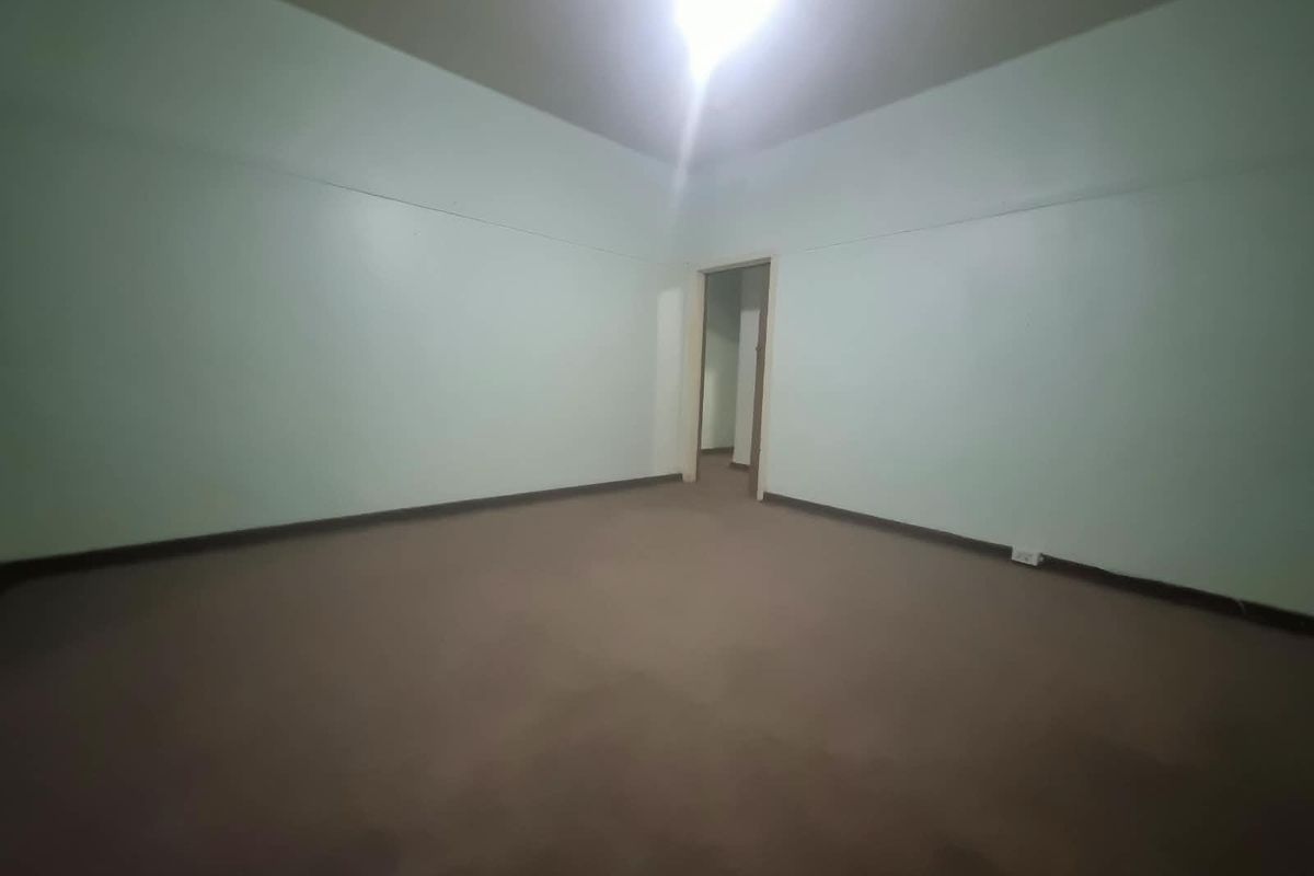 An empty, neutrally painted bedroom featuring carpeted flooring and a doorway leading to an adjacent space.