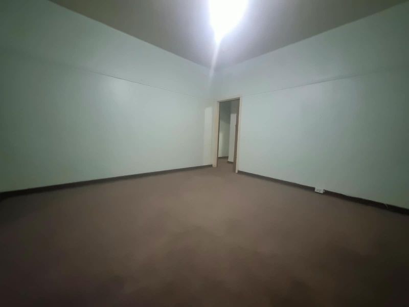 An empty, neutrally painted bedroom featuring carpeted flooring and a doorway leading to an adjacent space.