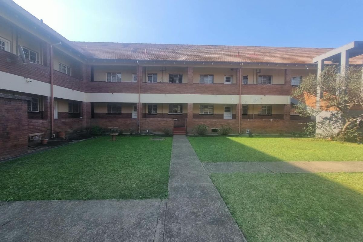 Rear view of a multi-story apartment complex featuring a central lawn, concrete pathways, and traditional brick facade with tiled roofing.